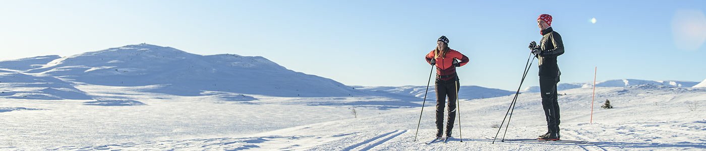 Kvinna och men åker Madshus längdskidor i vinterlandskap
